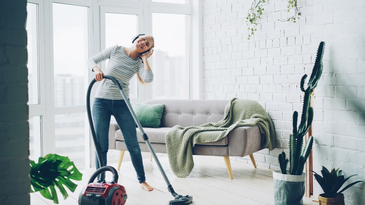 A woman vacuuming a bright modern living room with headphones on - Photo by Vitaly Gariev on Unsplash